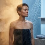 Athlete performing a contrast shower at home with visible thermometer and ice bucket nearby illustrating warm and cold phases of recovery